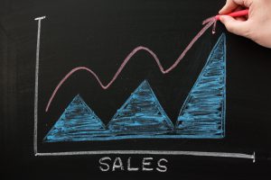 Hand drawing a red line for sales growth on a graph displayed on a blackboard.