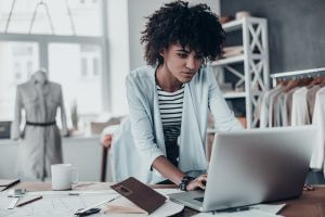 Beautiful young African woman working using computer while standing in workshop
