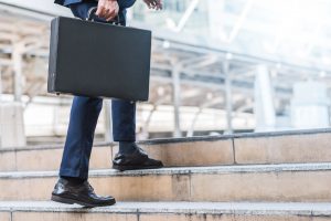 Close up shot of businessman holding leather briefcase while walking upward on the stair outdoor in city.