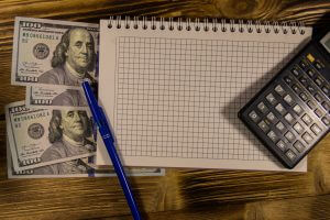 Notebook with dollars, pen and calculator on wooden desk. Financial concept
