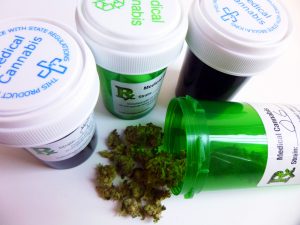 Close-up of four medical marijuana prescription containers. One opened container is in the foreground with cannabis bud falling out.