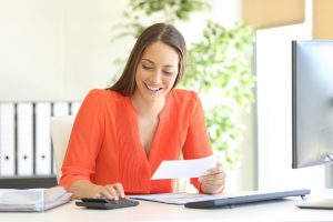 Businesswoman wearing orange blouse doing accounting and calculating with a calculator in a desktop at office