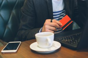 Cropped front view image of a young handsome businessman using laptop computer in cafe and doing payment with a creditcard