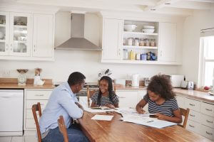 Father Helping Two Daughters Sitting At Table Doing Homework