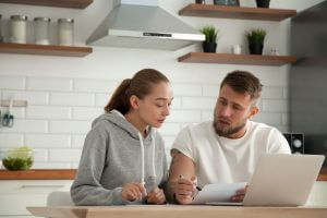 Focused young couple checking analyzing utilities bills sitting together at kitchen table, serious husband and wife reading bank loan documents with laptop, family managing finances planning expenses